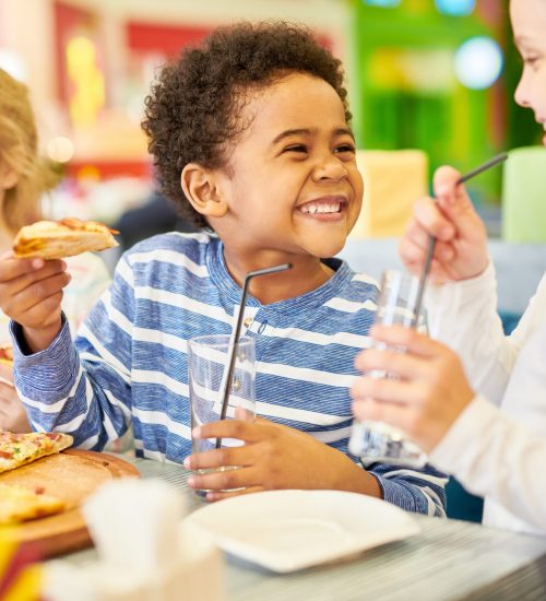 Happy Children in Pizzeria Colorful portrait of multi-ethnic group of children eating pizza enjoying awesome party in cafe, focus on African-American boy laughing happily